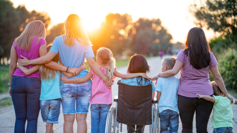 Children and adults, stand arms around each other against a sunset.