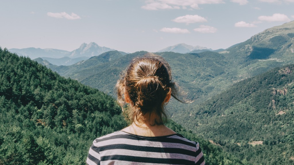 A woman with her hair tied in a ponytail stands looking across a mountain landscape.