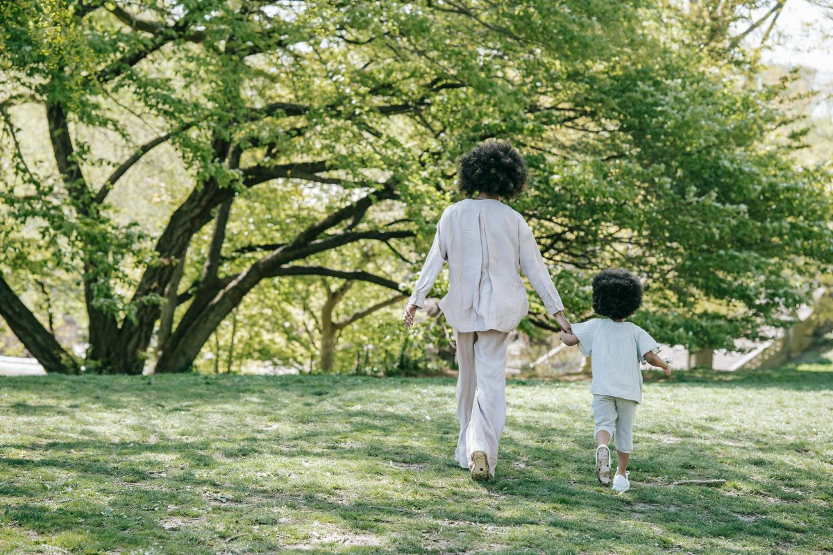 A mother and child hold hands, walking in the park