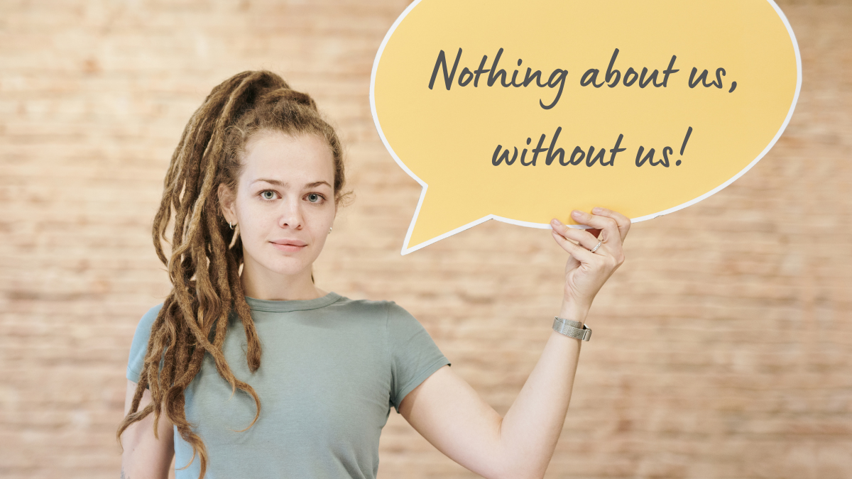A woman with dreadlocks holds up a speech bubble that reads "Nothing about us, without us!"