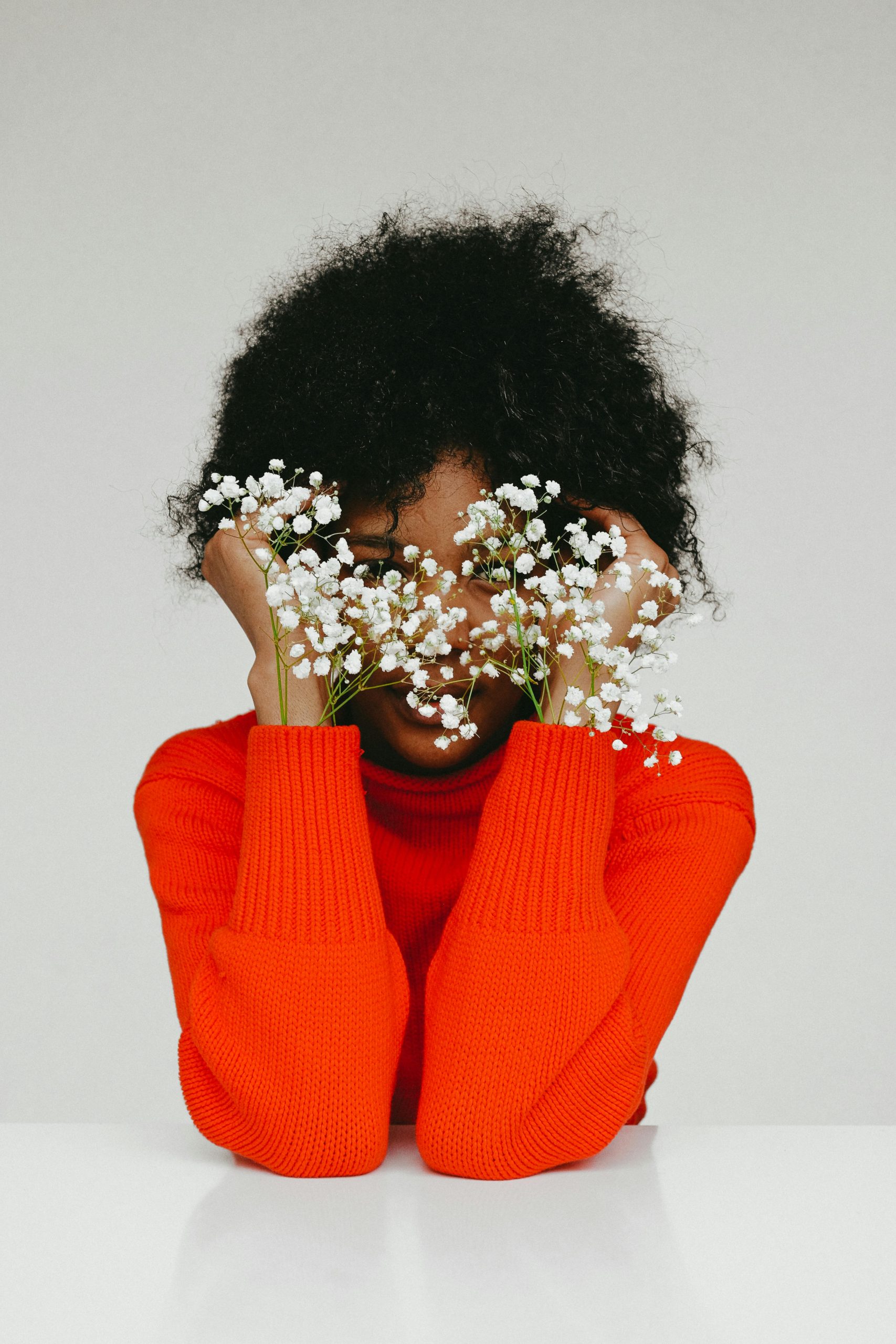 Woman in red sweater hiding her face behind white flowers
