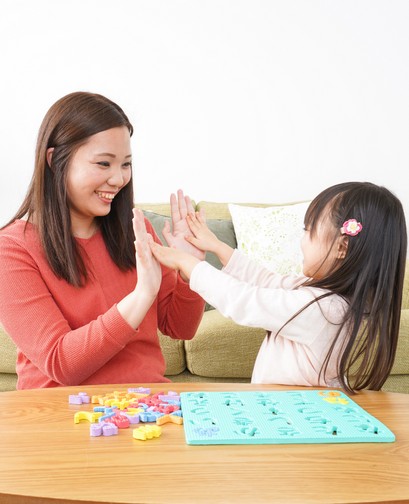 An Asian mother and young daughter are high-fiving and smiling as they sit behind a table that contains children's counting blocks.