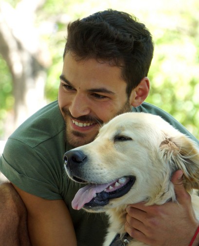 A young man is holding his dog, a golden retriever. He is smiling and looking away from the camera.