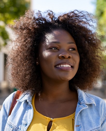 A woman of colour wearing a denim jacket is looking to the right and smiling.
