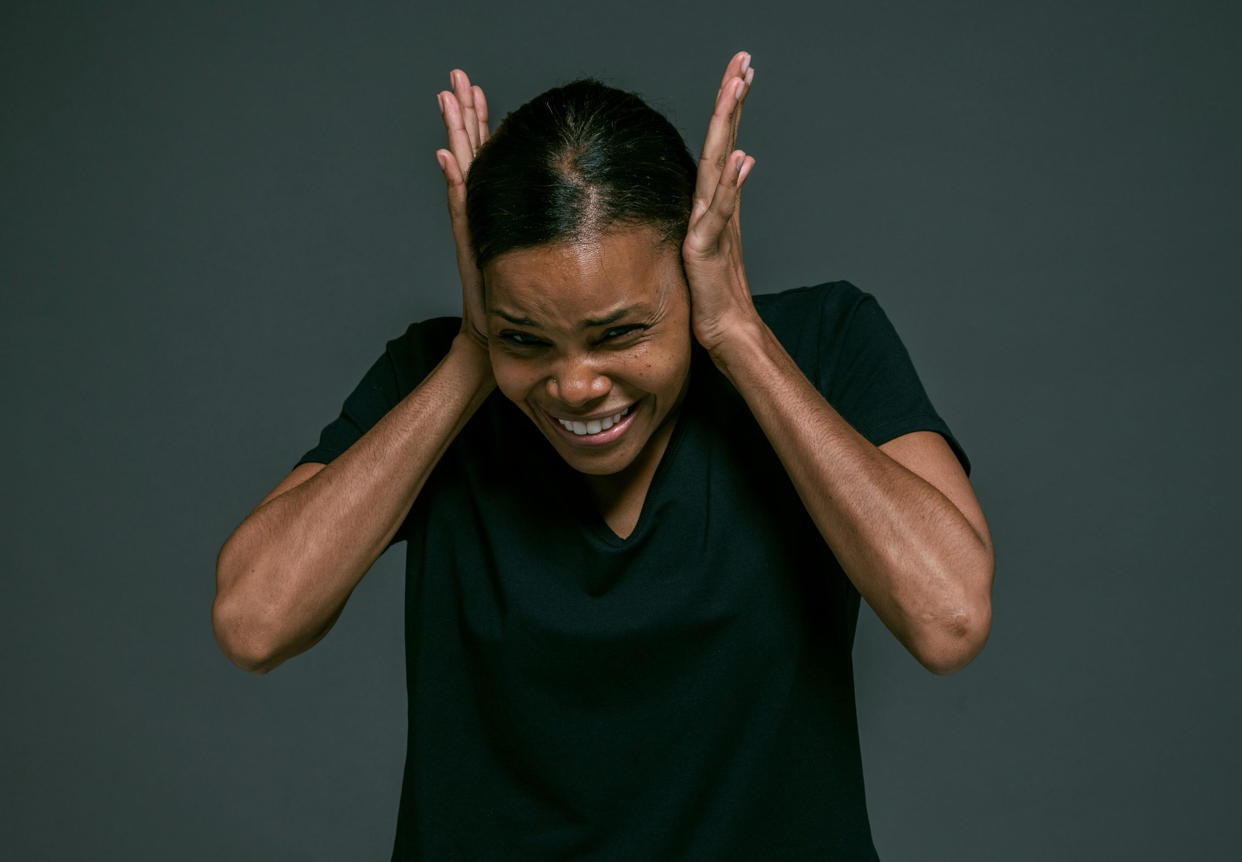 An African American woman stands covering her ears with a pained expression on her face.