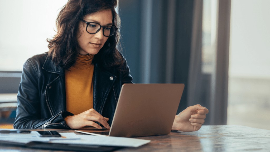 A woman wearing glasses is using a laptop.