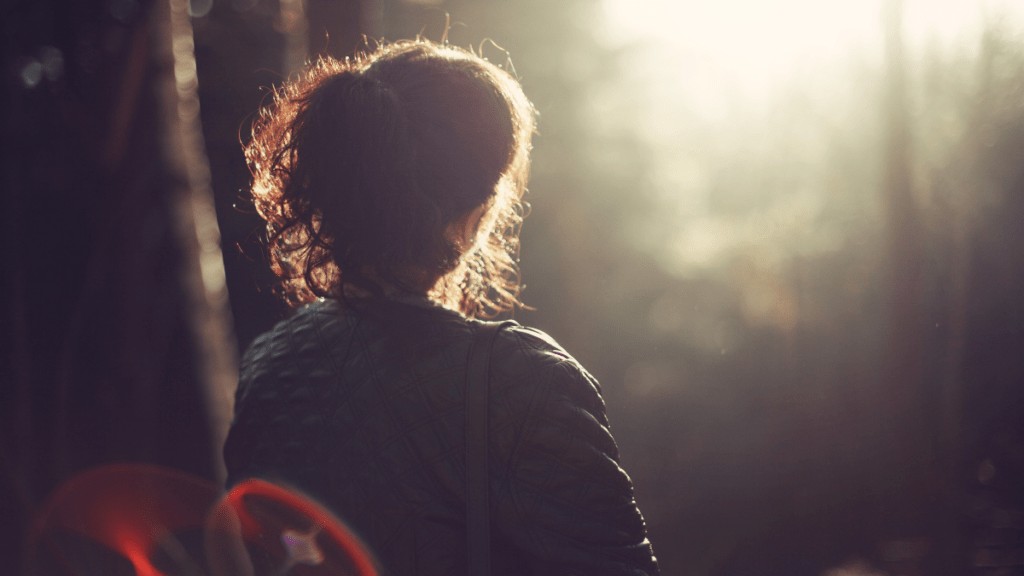 The silhouette of the back of a woman looking into a forest at golden hour.