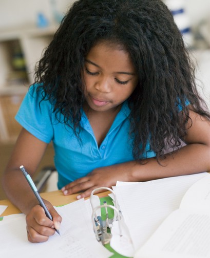 A young girl of colour is writing in a school binder.