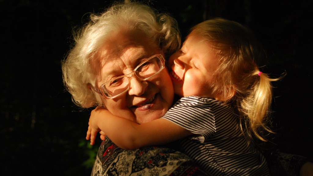 A grandmother embraces her young granddaughter. Both are smiling.