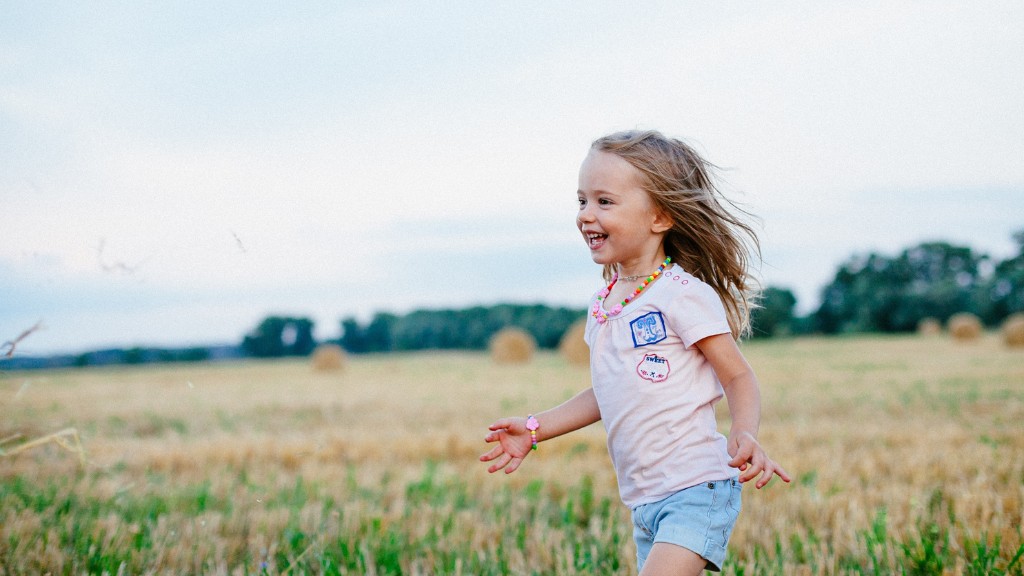 A young child wearing a tee shirt and shorts with long hair, running across a field. She is laughing.