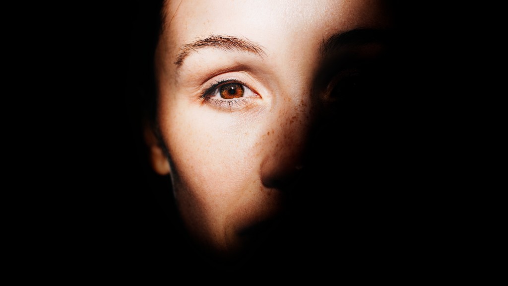 A woman's face, ensconced by shadows. She has one brown eye visible and she is looking directly at the camera.