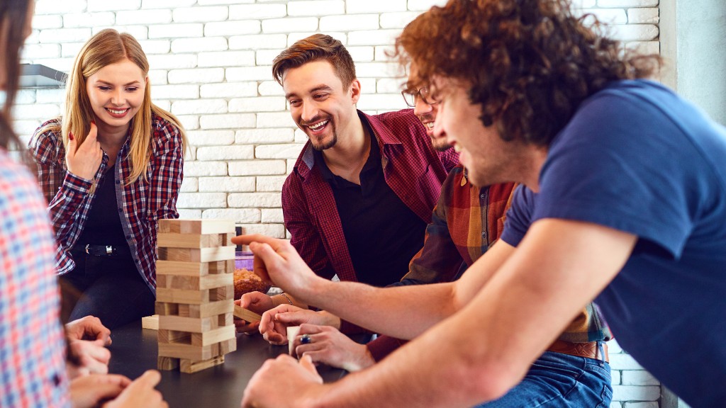 A diverse group of friends sitting around a coffee table are playing Jenga and smiling.