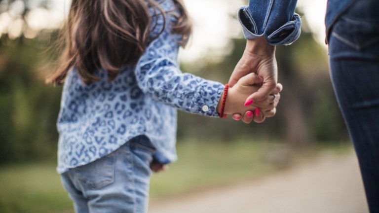 A mother and daughter are holding hands as they walk together.