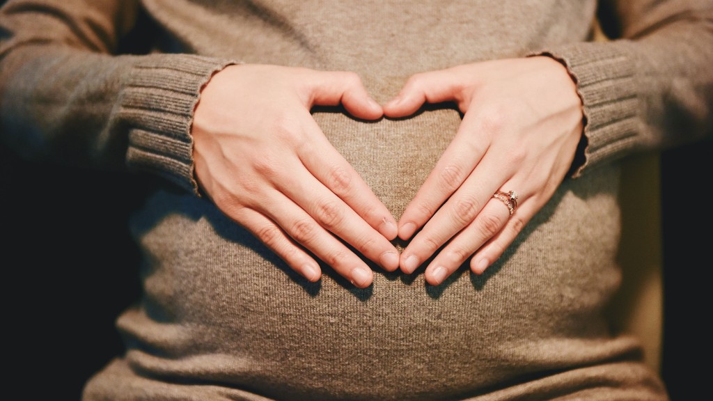 The belly of a pregnant woman, with her hands clasped in a heart formation over her belly.