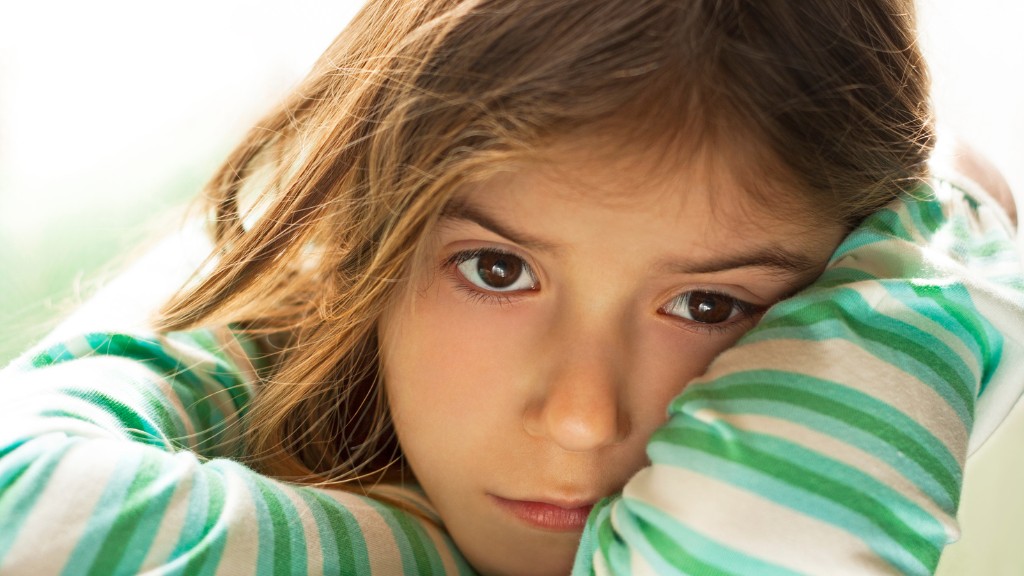 A young girl is looking sad and leaning her head onto her arm.