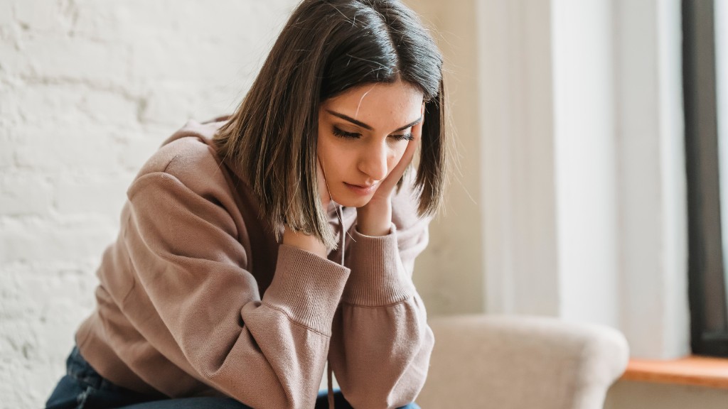 A woman with a bob haircut is sitting on a chair, her head clasped in her hands. She is looking down and not smiling.