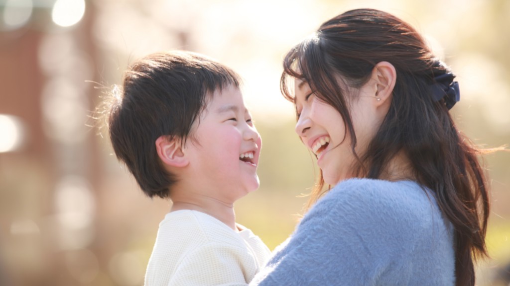 An Asian mother holds her young son in her arms. They are looking at each other and smiling joyfully.