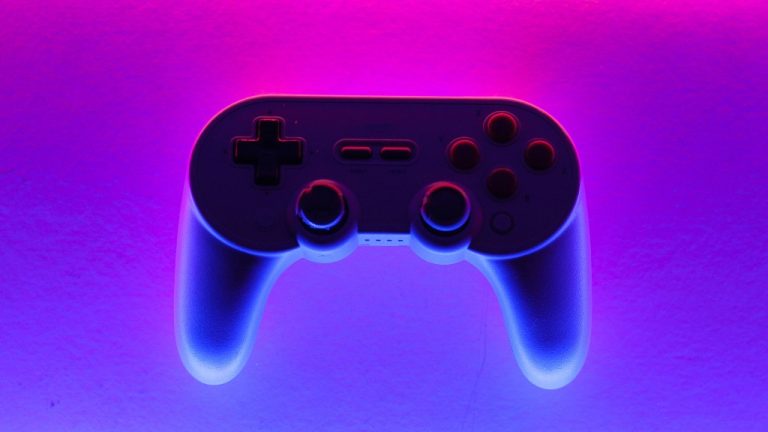 A gaming controller sits atop a pink, purple and blue background.