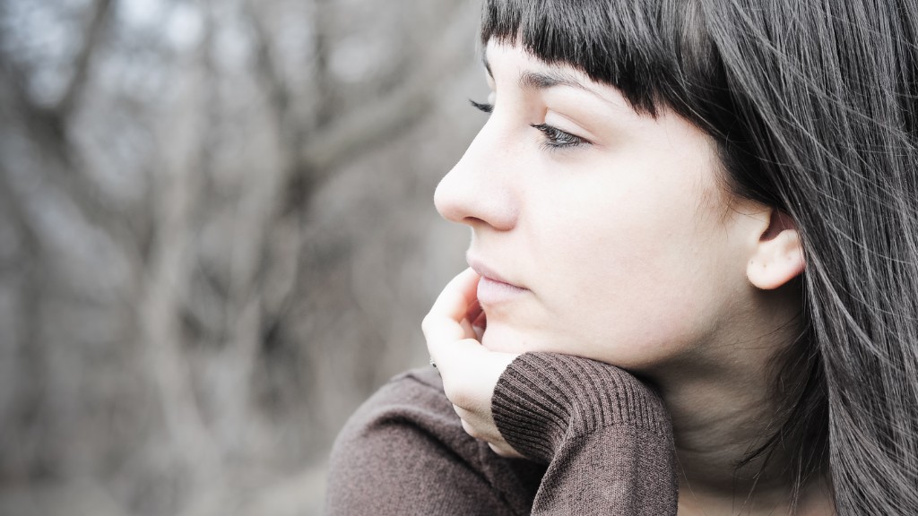 A woman with dark hair and a straight fringe sits with her chin in her hand, looking pensively to the left.