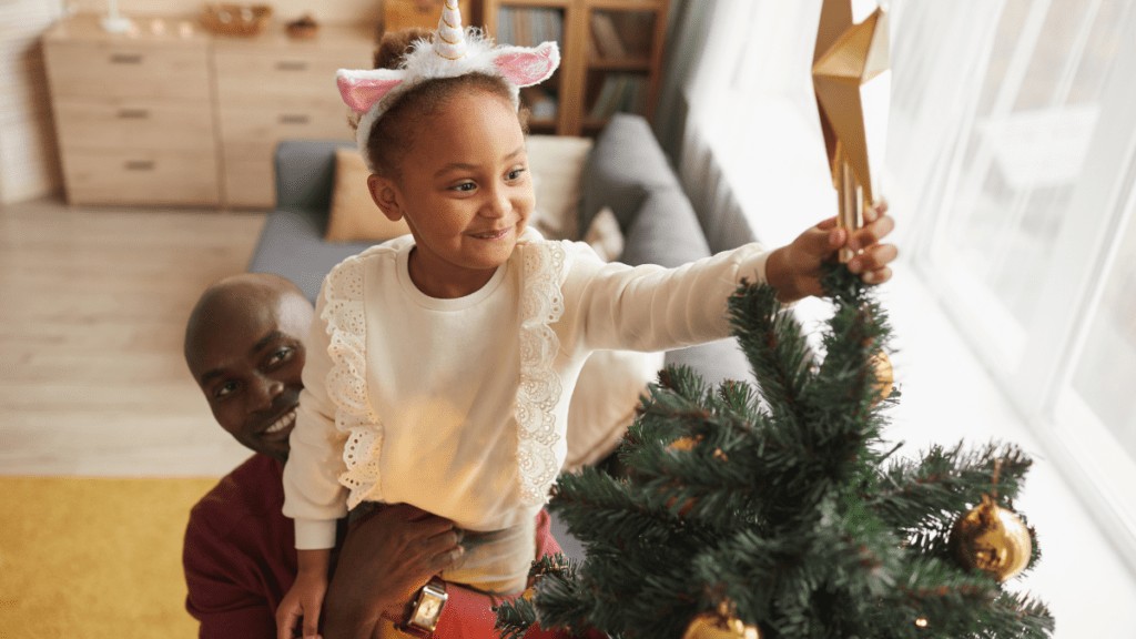 A father lifts his young daughter above his head to place a star on the Christmas tree.