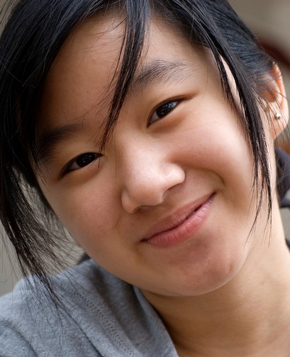 A young Asian woman with her hair in a ponytail is smiling at the camera.