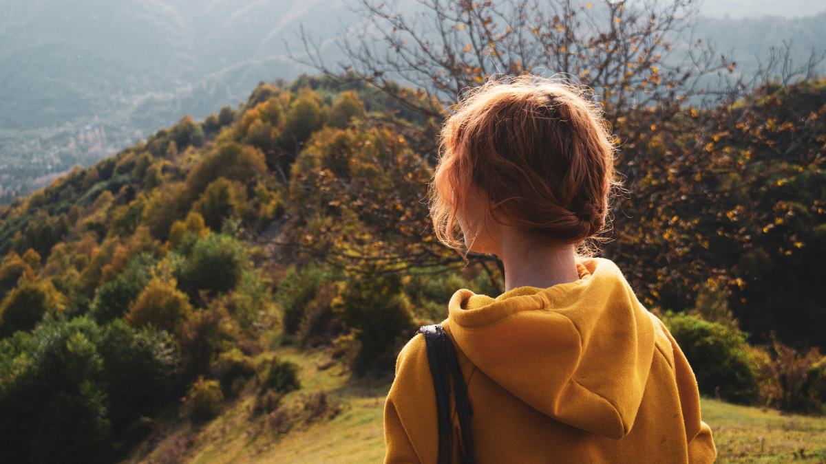 A photo looking over the shoulder of a young female adult as she faces a vast open landscape.