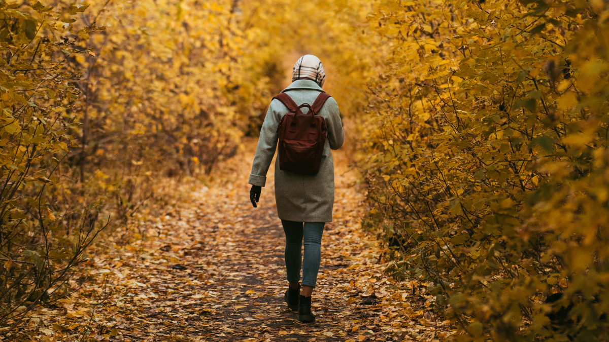 A photo of a teenage girl walking alone down a leafy track.