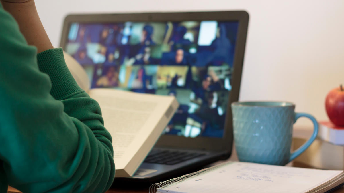 A woman sits in front of a computer as part of an online meeting.