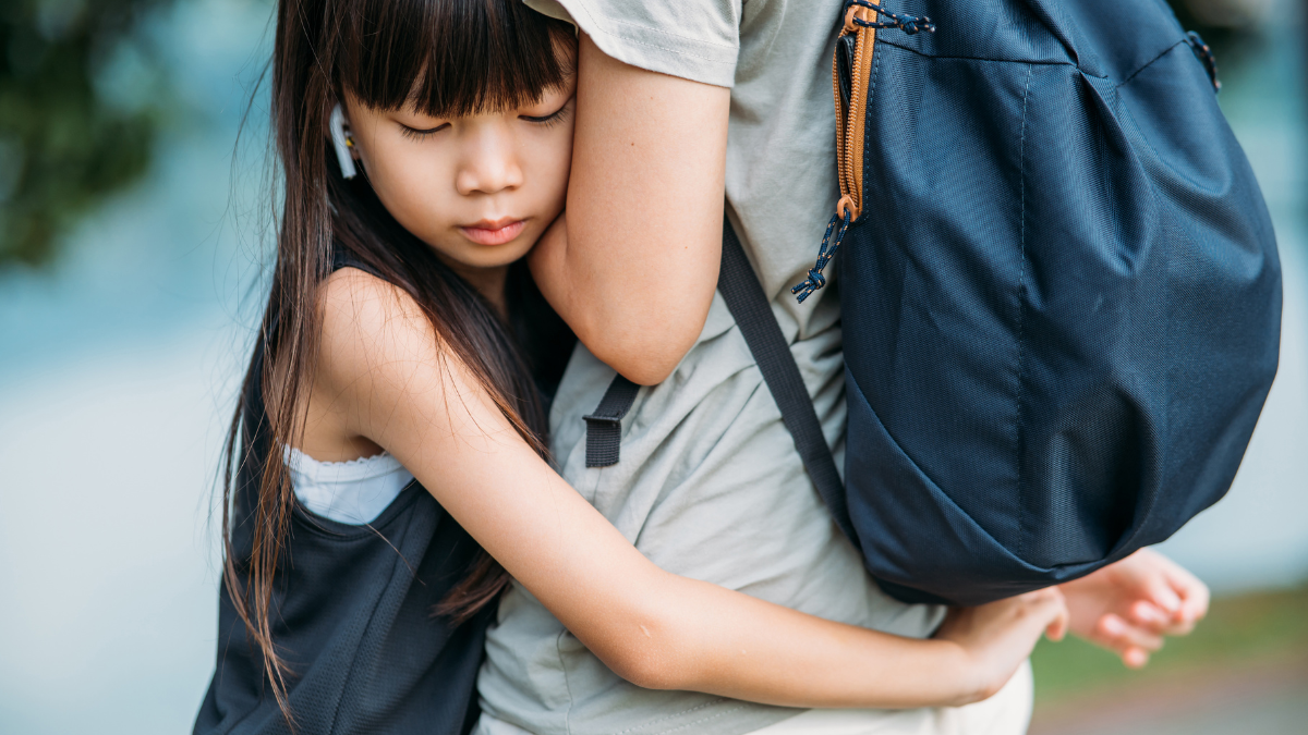 An Asian primary school girl clings on around her parent's waist.