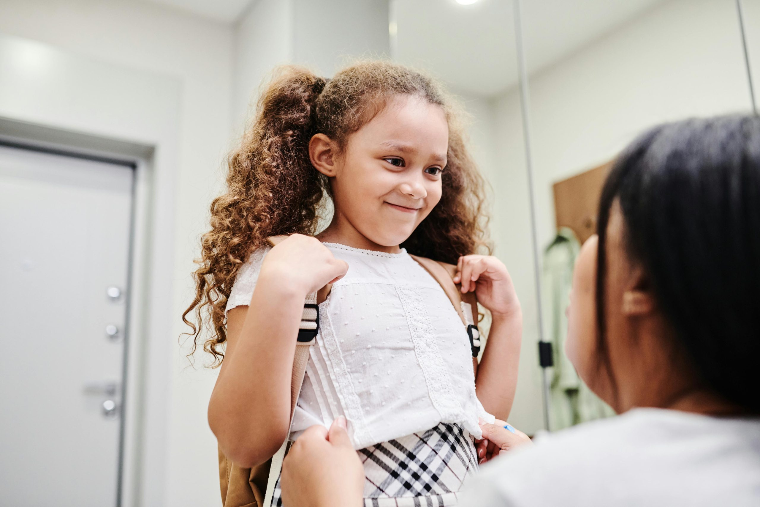 Little Girl with Backpack Smiling While Looking at her mother