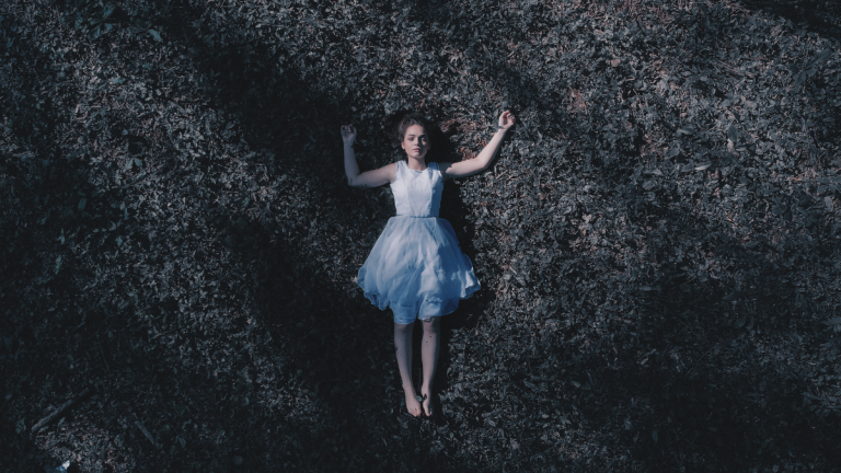 A birds eye view of a woman in a white dress lying flat on her back on the ground