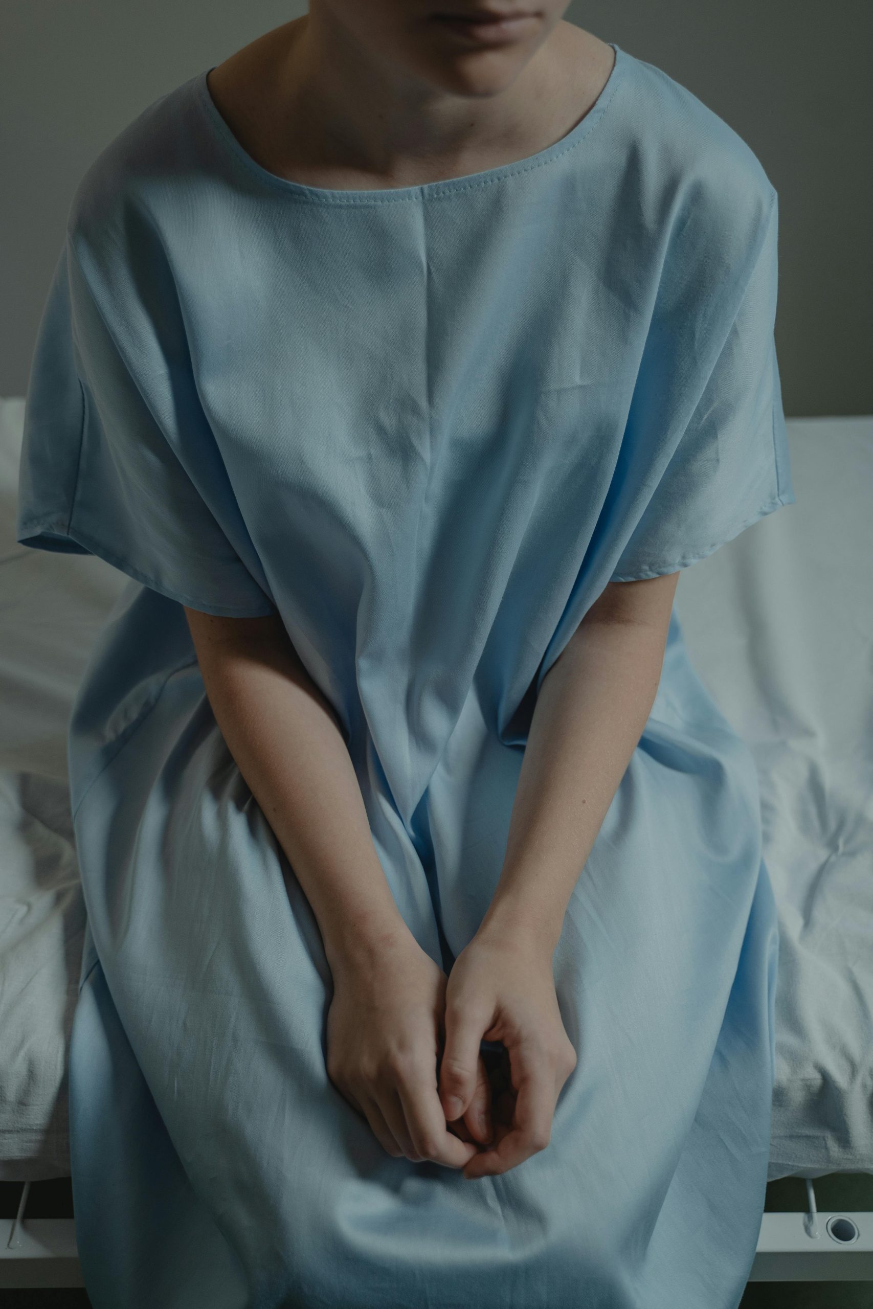 A person sitting on the edge of a hospital bed in a gown