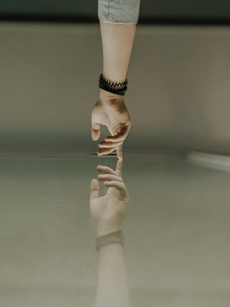 A hand reaching to touch a mirrored surface