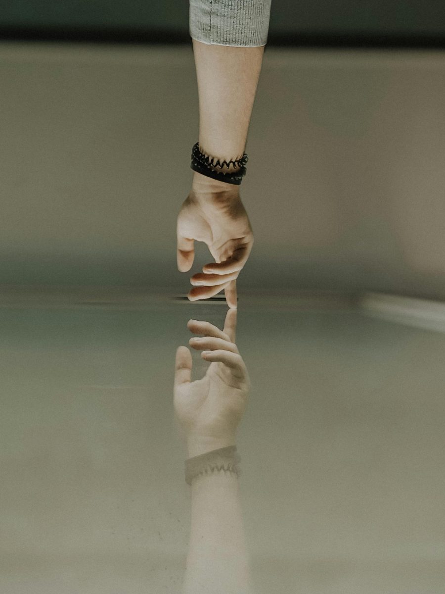 A hand reaching to touch a mirrored surface
