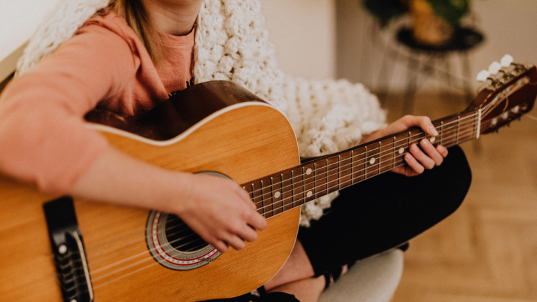 A close up photo of the torso of a woman playing the guitar at home.