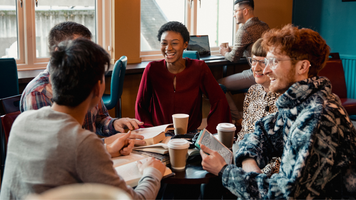 A diverse group of young adults sit at a table in a cafe.