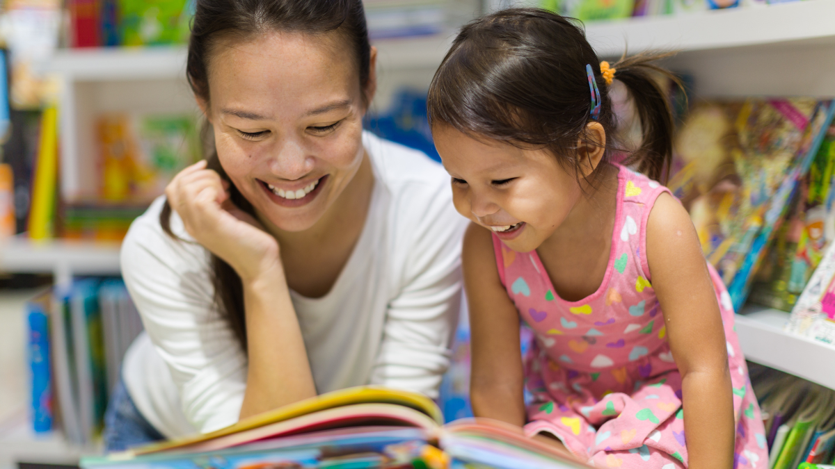 Photo of an Asian mother and child looking at a picture book together, smiling.