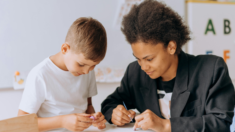 A photo of a teacher helping a primary-school-aged boy in a classroom