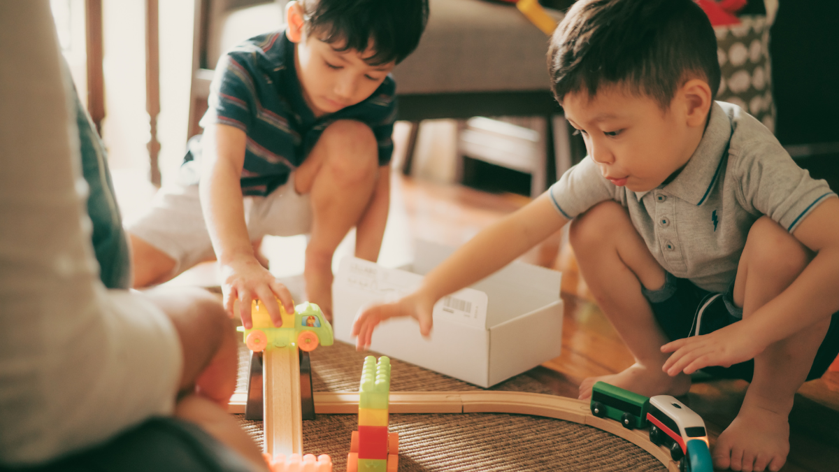 Photo of two young boys playing together with a train set on a rug.