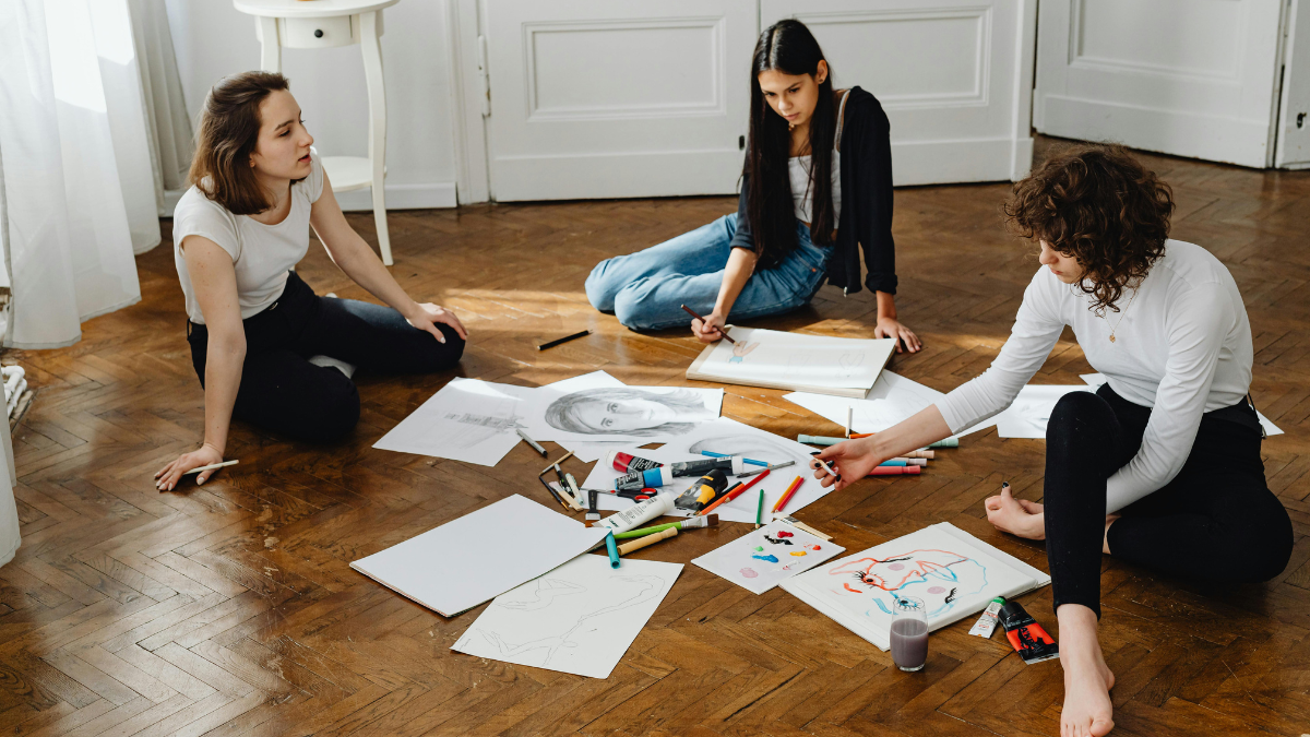 Photo of group of women, sitting on the floor and creating artworks.