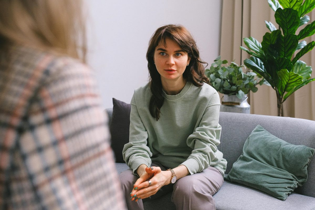 A photo of a thirty-year-old Caucasian woman with brown hair, sitting on a sofa.