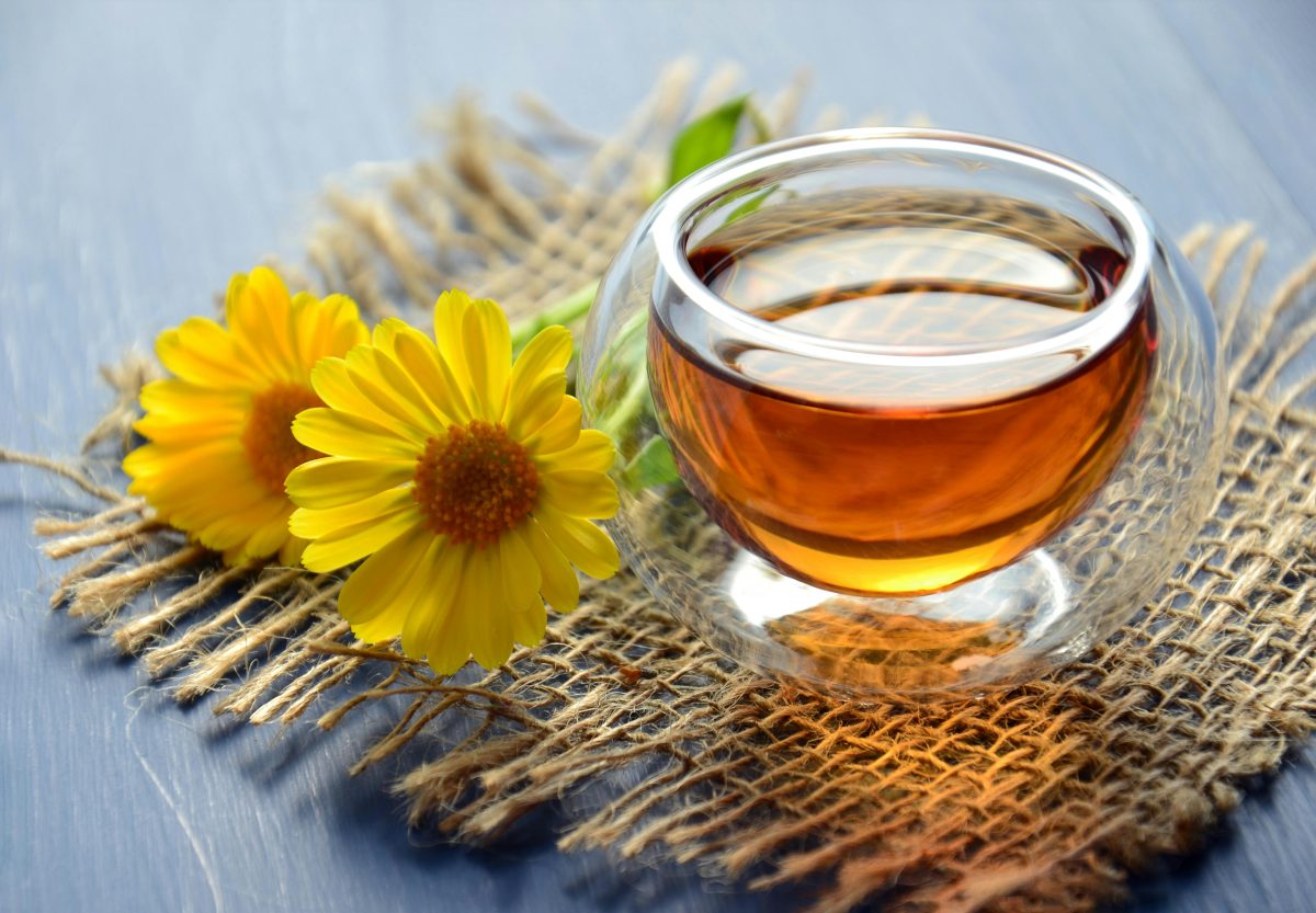 A close-up of a glass of tea on a hessian coaster, next to a couple of yellow daisies.