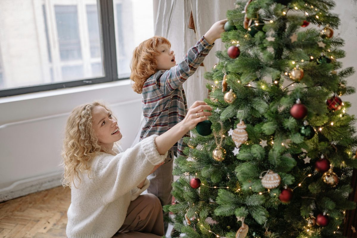 A photo of a mother and her toddler hanging ornaments on a Christmas tree.
