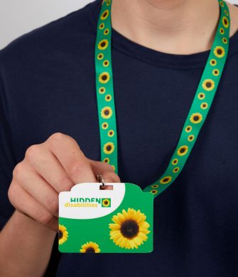 A lady holds up the Yellow Sunflower Invisible Disabilities lanyard